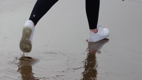 girl in white sports trainers running through wet soggy sand to avoid getting wet as footprints disappear instantly