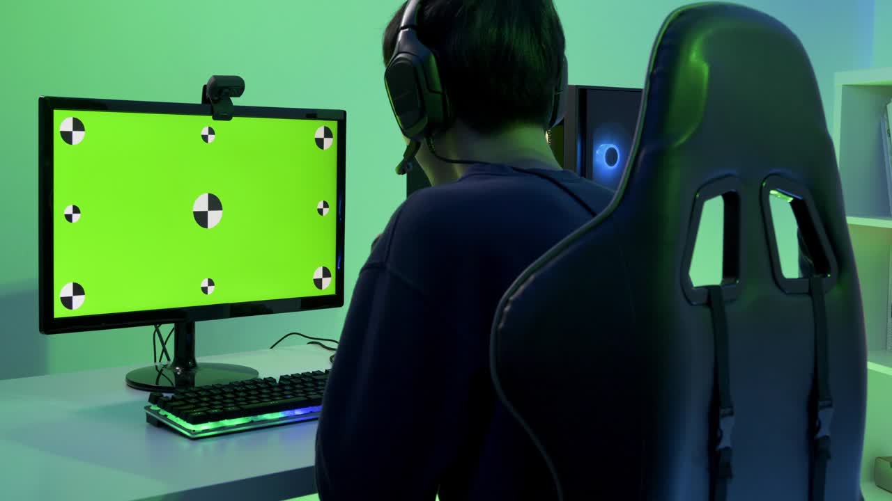 Male gamer playing game at home. Focus on green screen background inside monitor.