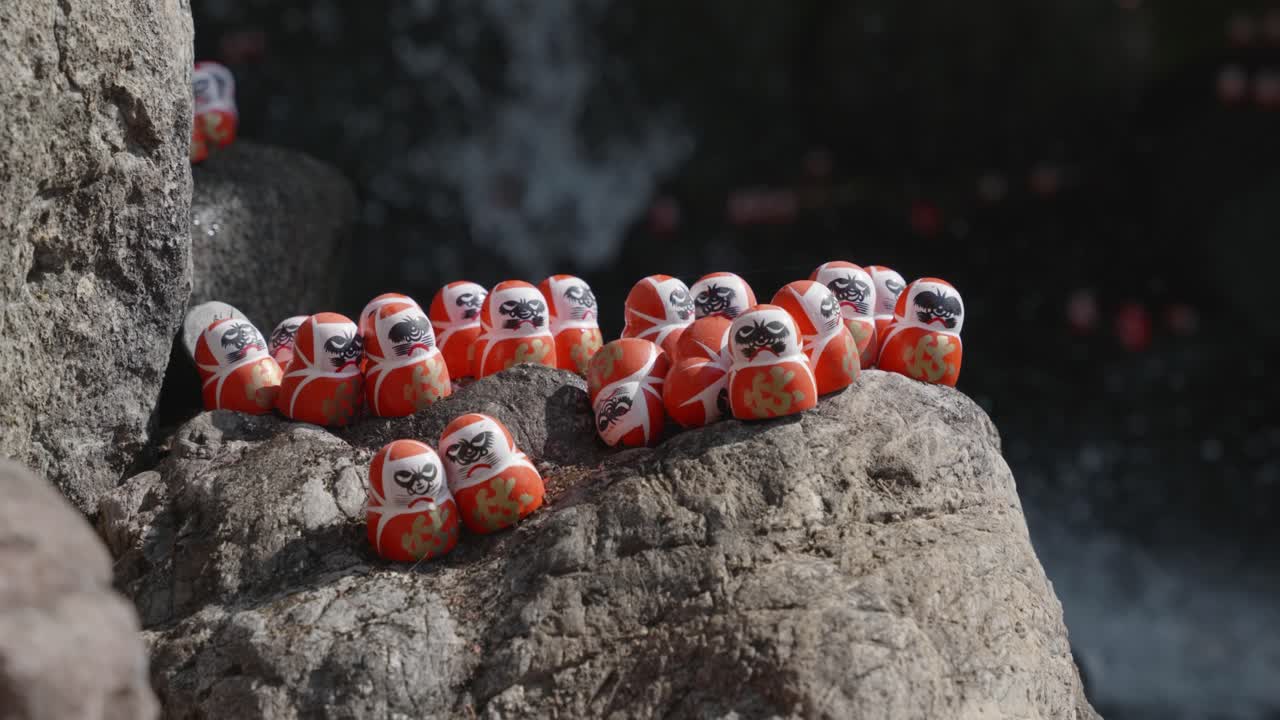 Small red daruma dolls on a stone by a waterall on a sunny day in Katsuoji Temple, Osaka. Japan