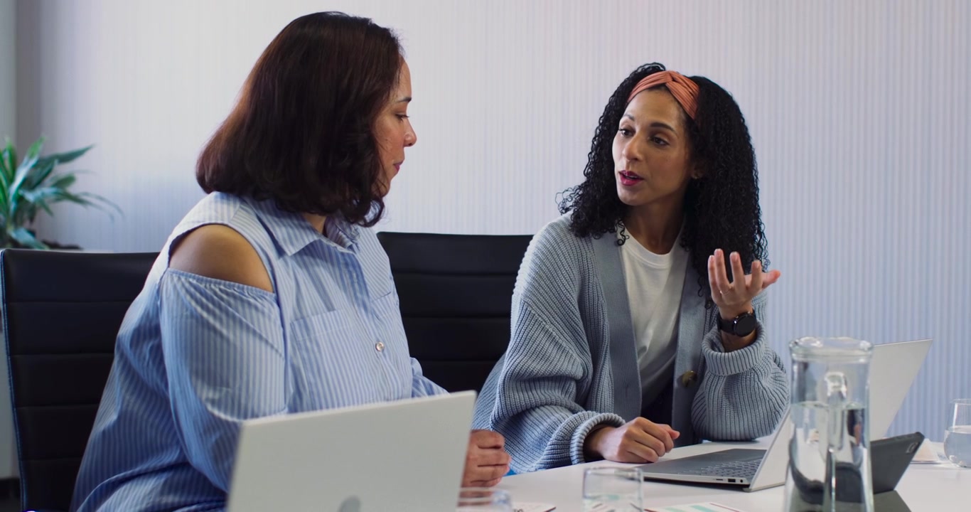 Due donne afroamericane che esaminano due computer portatili, collaborando e gesticolando a un tavolo riunioni