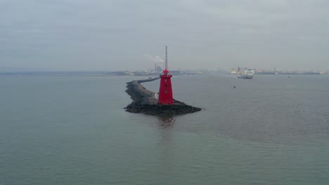 Drone-parallax-around-red-Poolbeg-lighthouse-with-rock-platform-leading-to-iconic-symbol