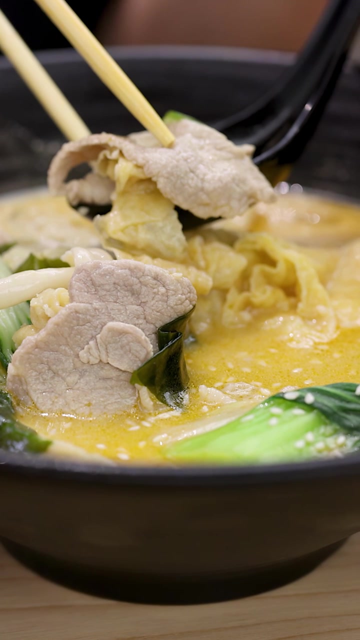 Primo piano di una zuppa di noodle piccante e calda mentre un commensale solleva carne e un raviolo con le bacchette.