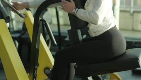 the girl sits down on the training machine and prepares for sports exercise