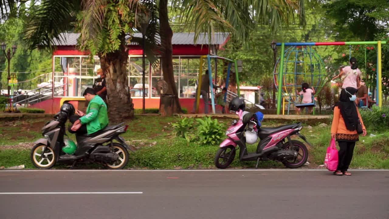 a man in a "Grab" driver jacket sits on a motorbike next to city park, Semarang, Central Java, Indonesia on June 10, 2022
