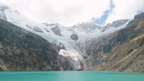 drone flying forward above turquoise glacial lake while tilting up to reveal snow-covered peaks on santa cruz trek
