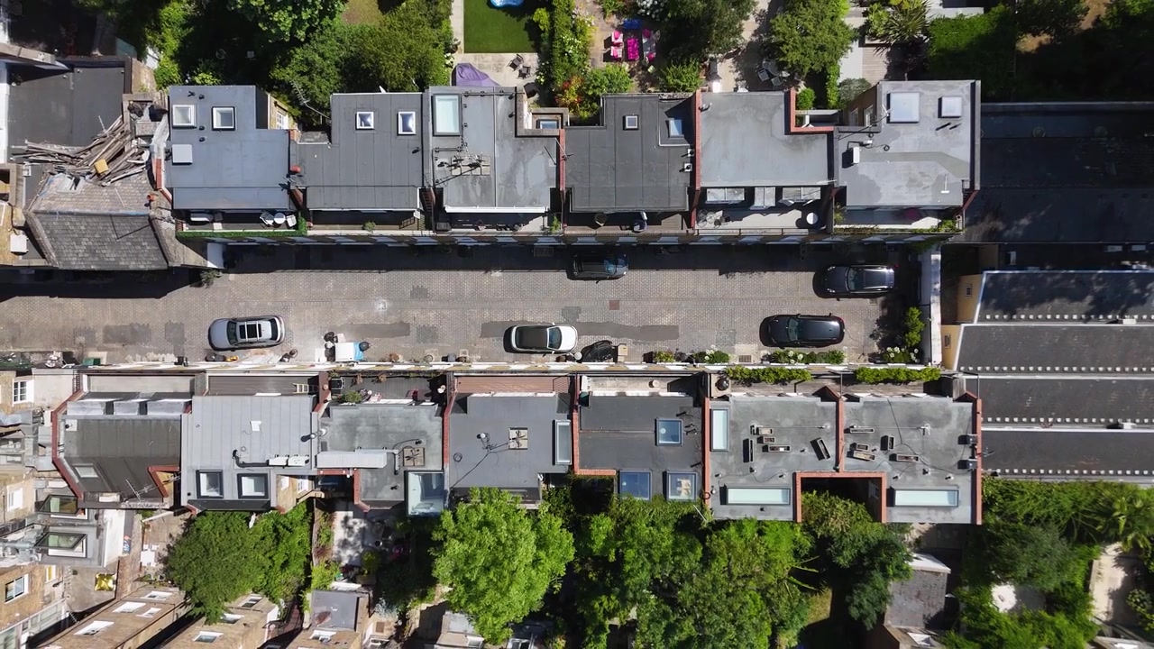 Vista dall'alto di una strada privata tra file di case con tetto piatto, dotate di lucernari, terrazze sul tetto e auto parcheggiate