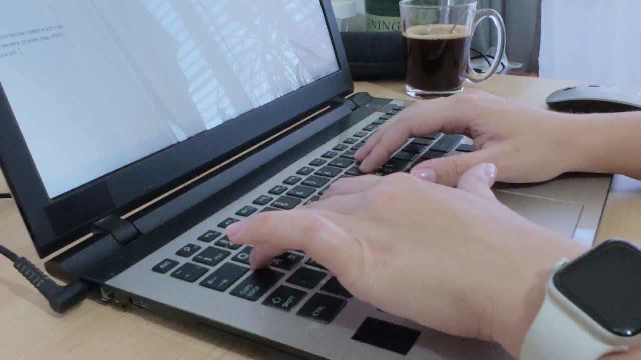 Hands typing on laptop keyboard, with a fresh cup of coffee and smartwatch on desk