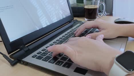 hands typing on laptop keyboard, with a fresh cup of coffee and smartwatch on desk