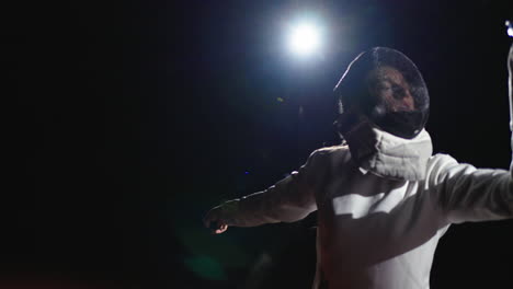 a woman in a white fencing uniform is posing with a sword, wearing a mask, black background.