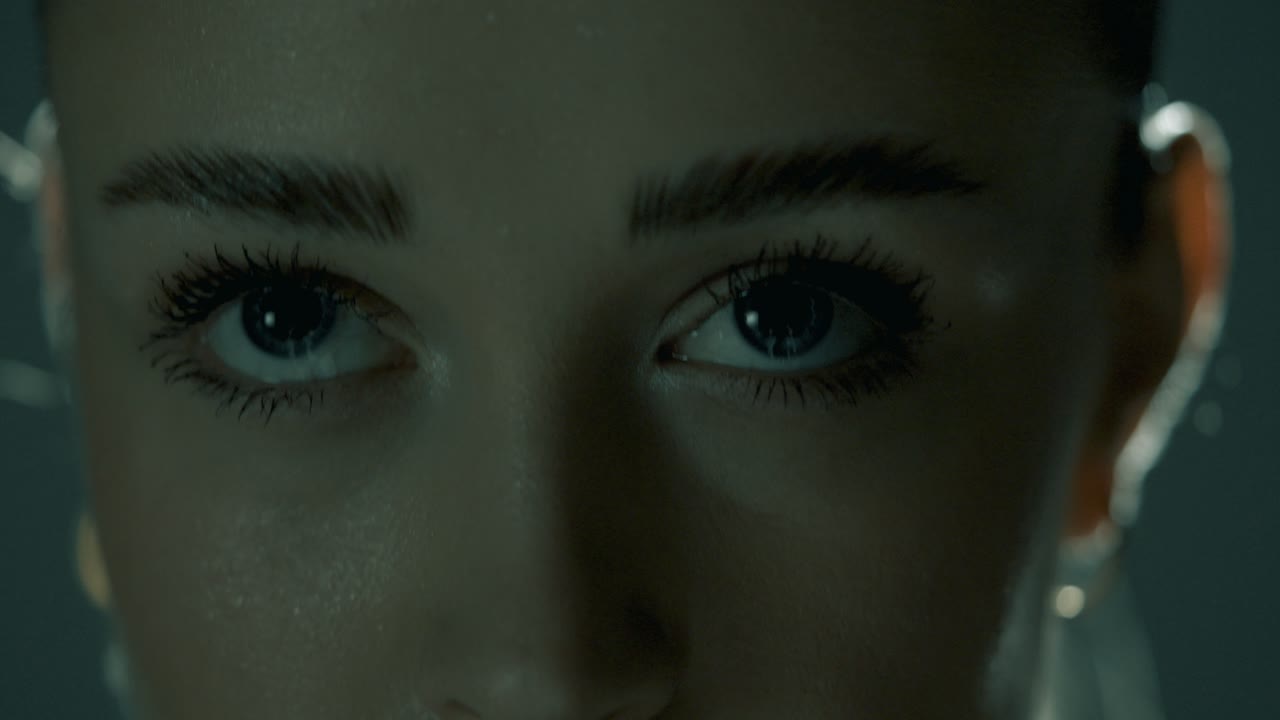 Tight closeup capturing a woman’s intense eyes during training as the camera lowers to her lips, revealing sweat-drenched skin and breath control, framed in soft cinematic lighting and sharp detail
