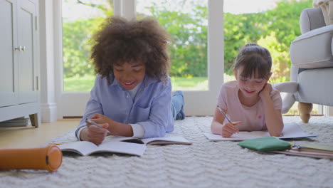 boy and girl lying on rug in lounge at home doing school homework together