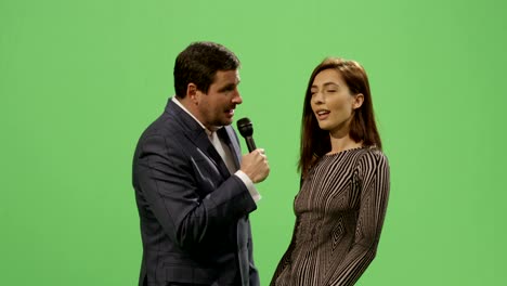 un reportero de medios con un micrófono está tomando una entrevista de una mujer con un vestido en una pantalla verde simulada en el fondo.