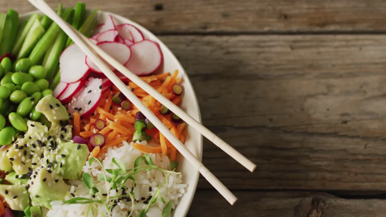 Composition of bowl of rice, salmon and vegetables with chopsticks on wooden background