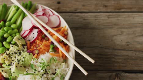 Composition-of-bowl-of-rice,-salmon-and-vegetables-with-chopsticks-on-wooden-background