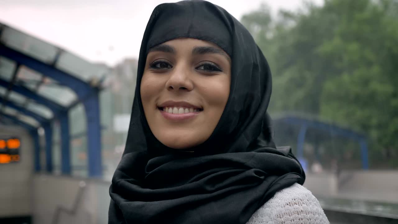 Young dreaming muslim woman in hijab is smiling on railway station, religion concept, urban concept