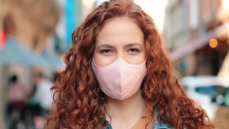 close-up view of redheaded woman wearing mask looking at camera and smiling in the street