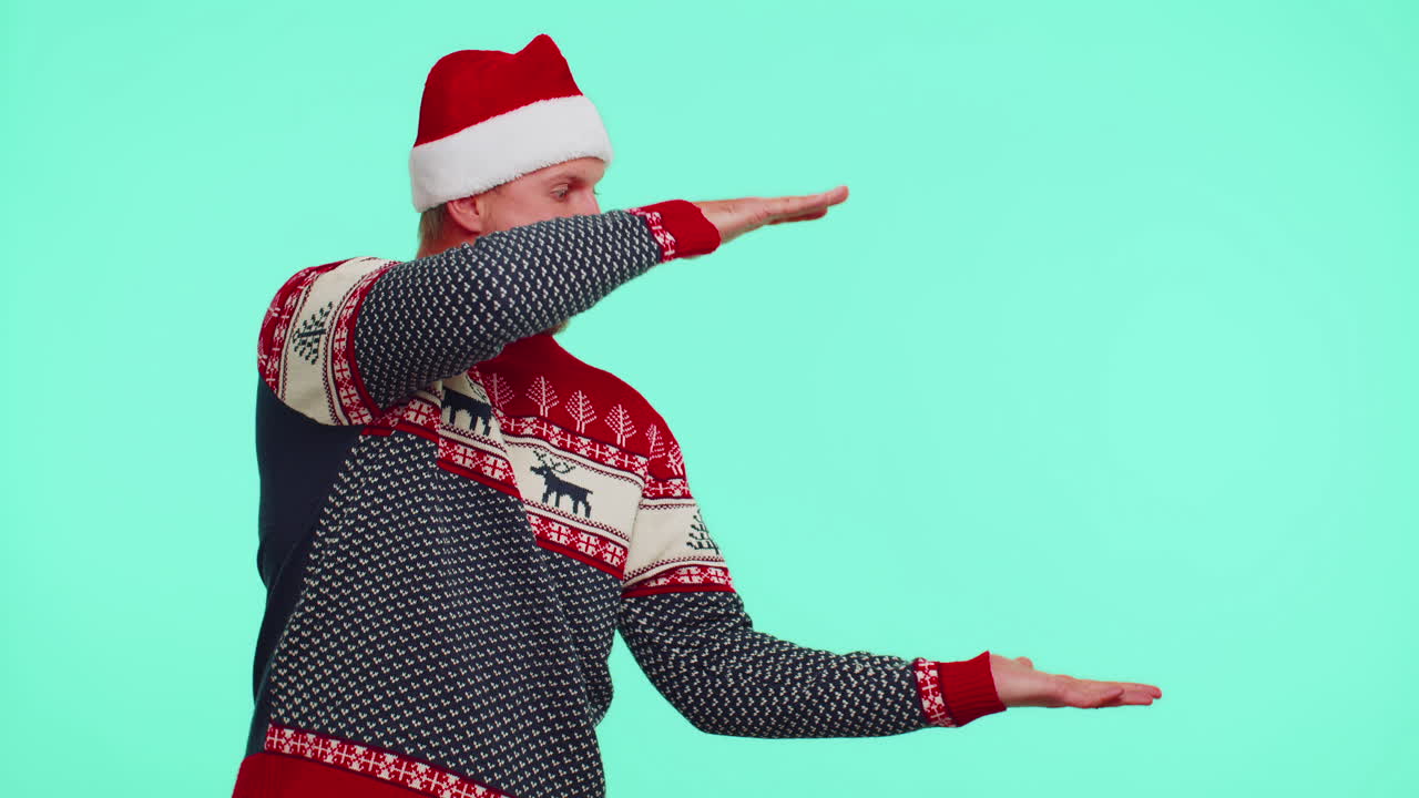 남자가 빨간 새해 스웨터를 입고 사이 엄지손가락을 올리고 빈 광고 공간을 가리키고 있습니다.