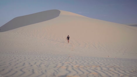 Hombre-Vestido-De-Negro-Corriendo-Por-Las-Dunas-De-Arena-Blanca-En-Mui-Ne,-Phan-Thiet,-Vietnam