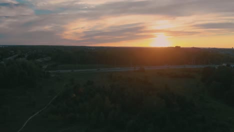 Slow-aerial-flight-towards-a-highway-outside-nepean-city,-ontario-at-sunset-with-the-sun-shining-over-the-hill-and-trees