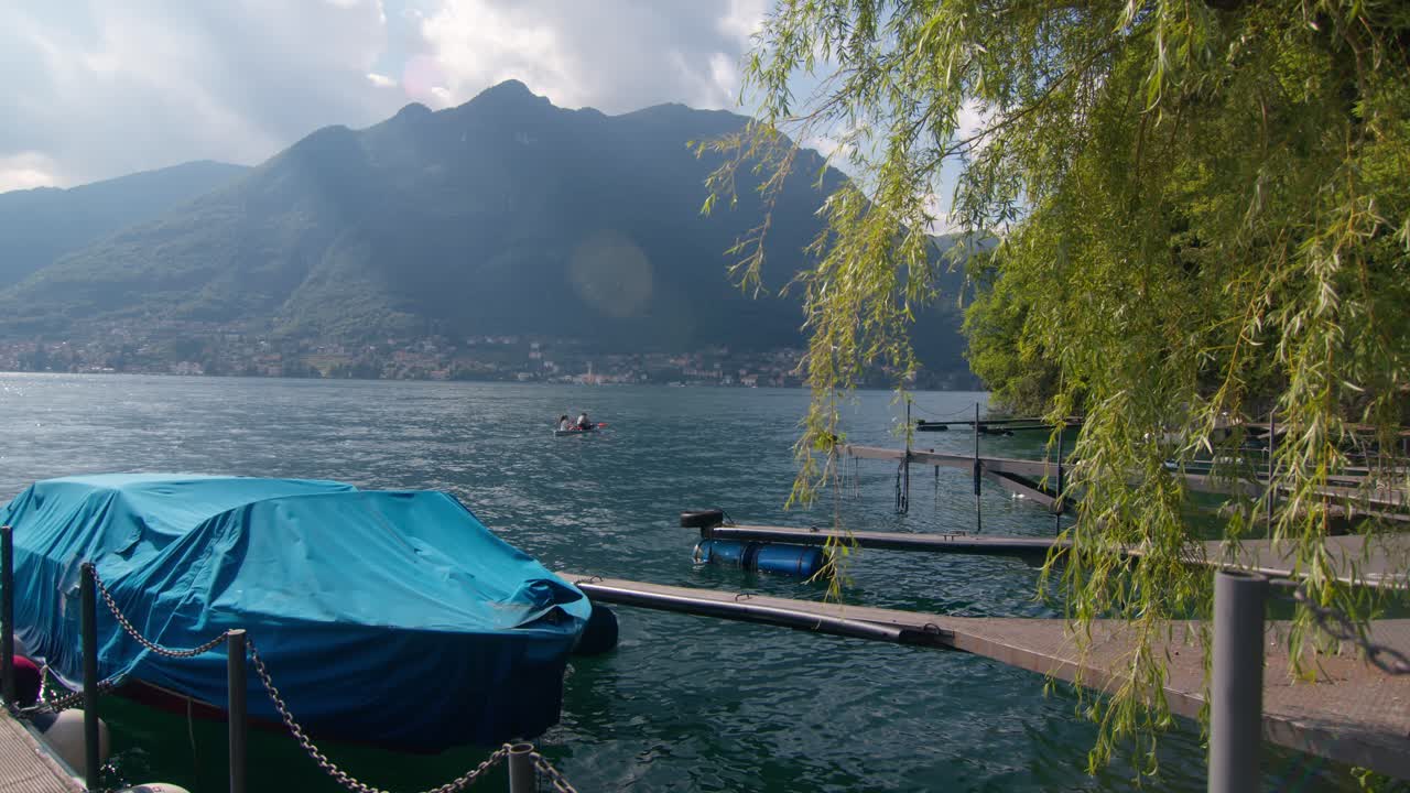 Wide shot of Lake Como, Italy (Lago di Como, Italia) with docked speedboat and couple kayaking far in the distance