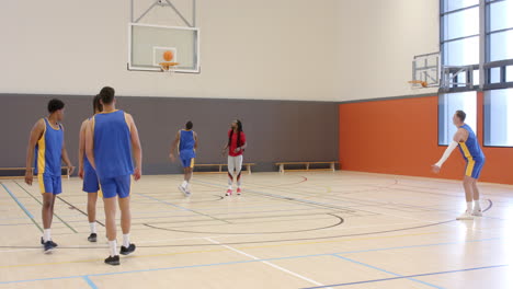multiracial male basketball players throwing ball with coach giving instructions to players in gym