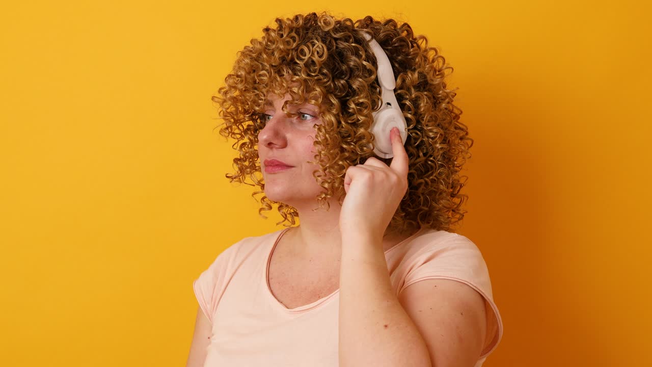 무선 헤드폰으로 음악을 듣고 노란색 배경에서 재미를 느끼는 즐거운 30대 여성