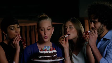 group of smiling friends blowing candle while celebrating birthday in bar