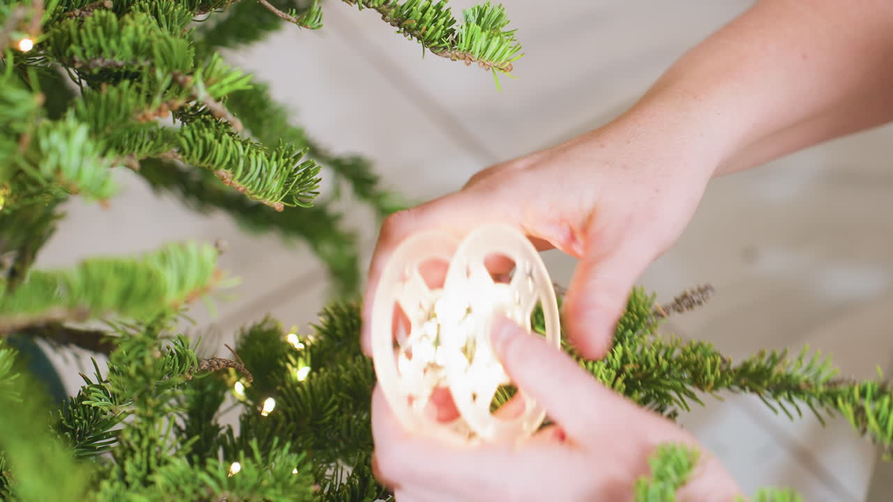 Hand carefully tying lights on vibrant green Christmas tree branches, showcasing holiday preparation spirit with close-up view of twinkling lights and textured pine needles in cozy festive setting