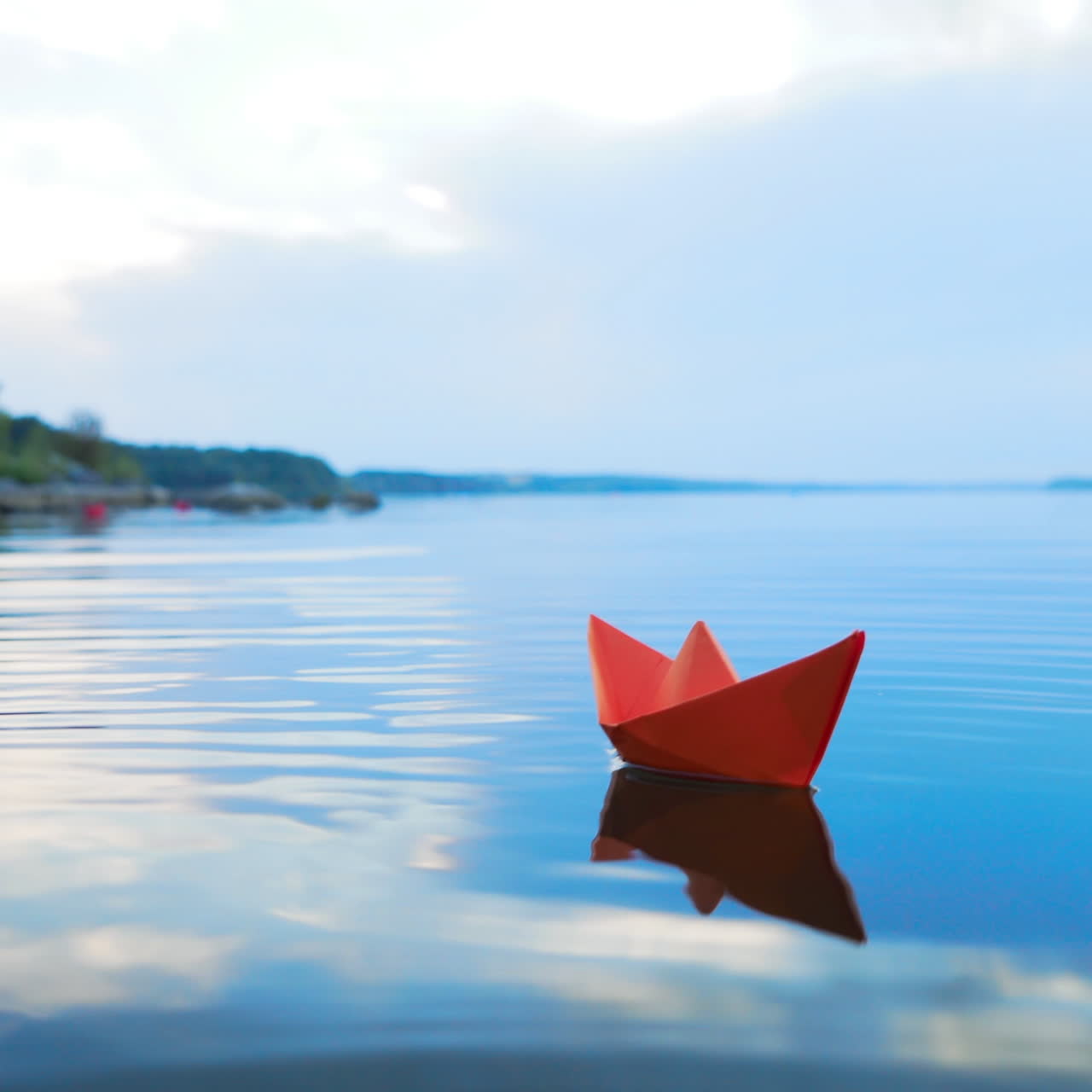 Ship of red paper floating in the blue river at clear day under the blue sky. One paper boat swims on the calm lake in summer