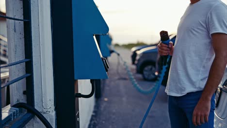 joven irreconocible cargando su coche eléctrico en una estación de carga pública