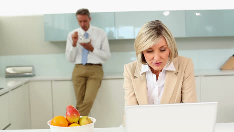 Mujer-De-Negocios-Usando-Una-Computadora-Portátil-Mientras-Su-Esposo-Come-Cereal-Antes-De-Trabajar