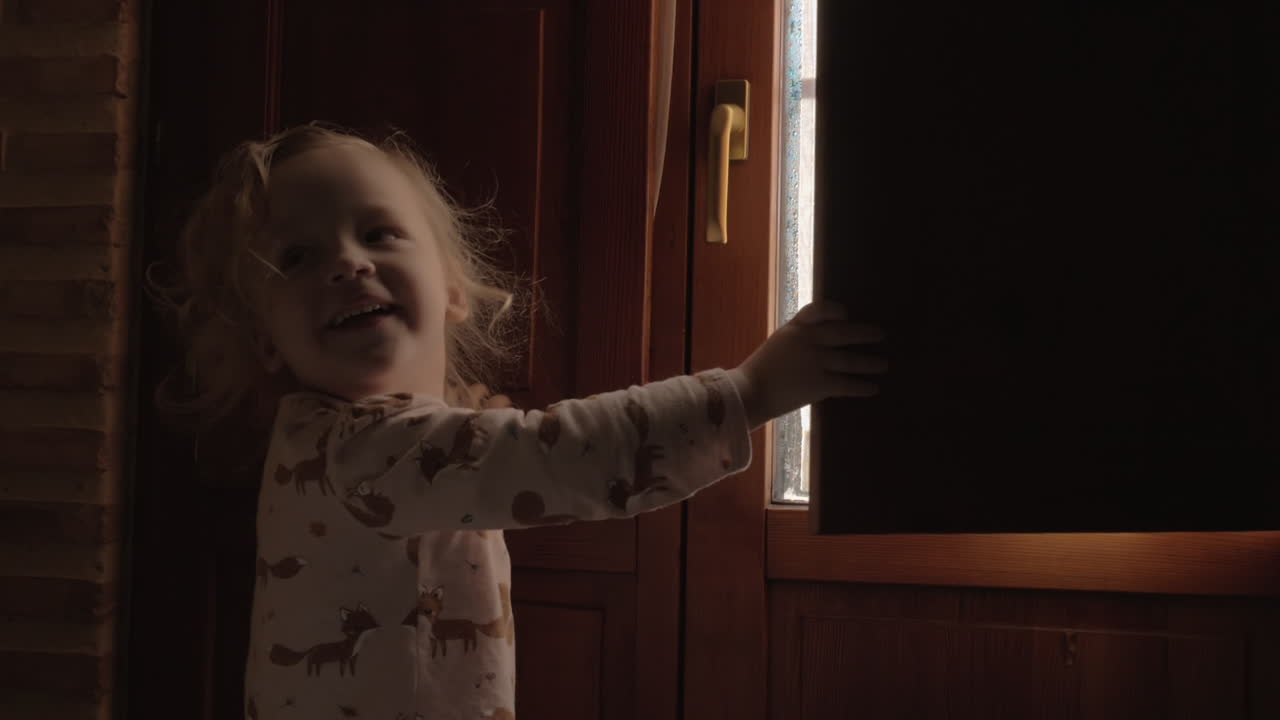 Little girl is happy with new day and opening shutters in the morning