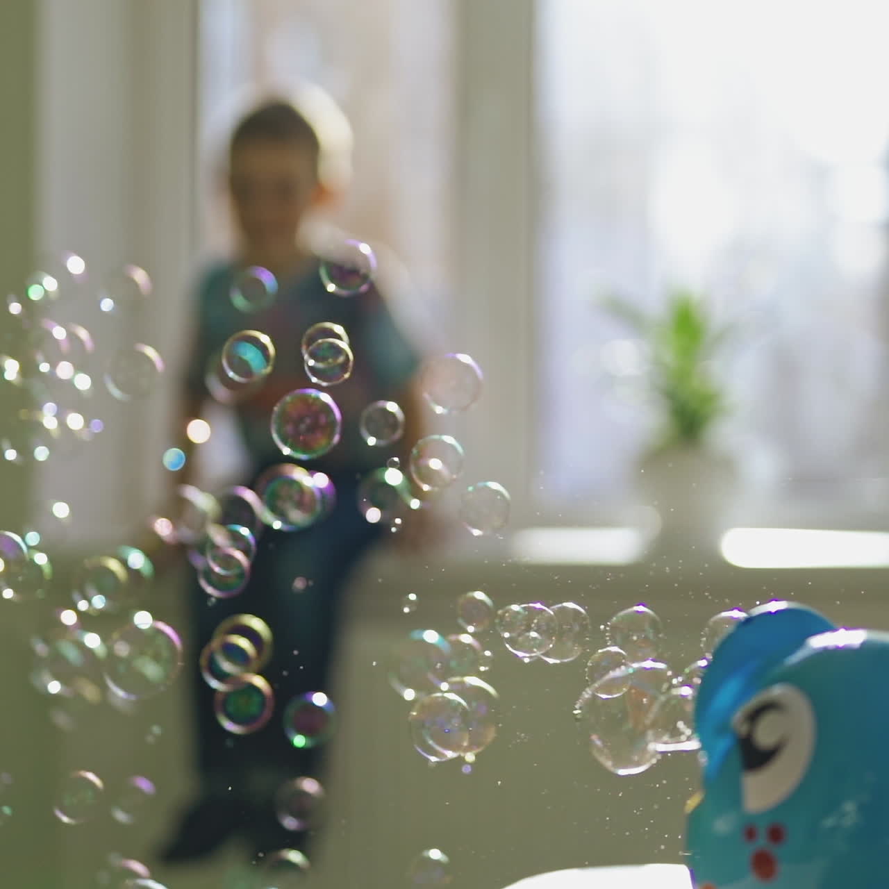 Colorful circle bubbles flying in the room on the blur background with a boy. Special device for creating soap bubbles on the table. Soap bubbles show inside the room.