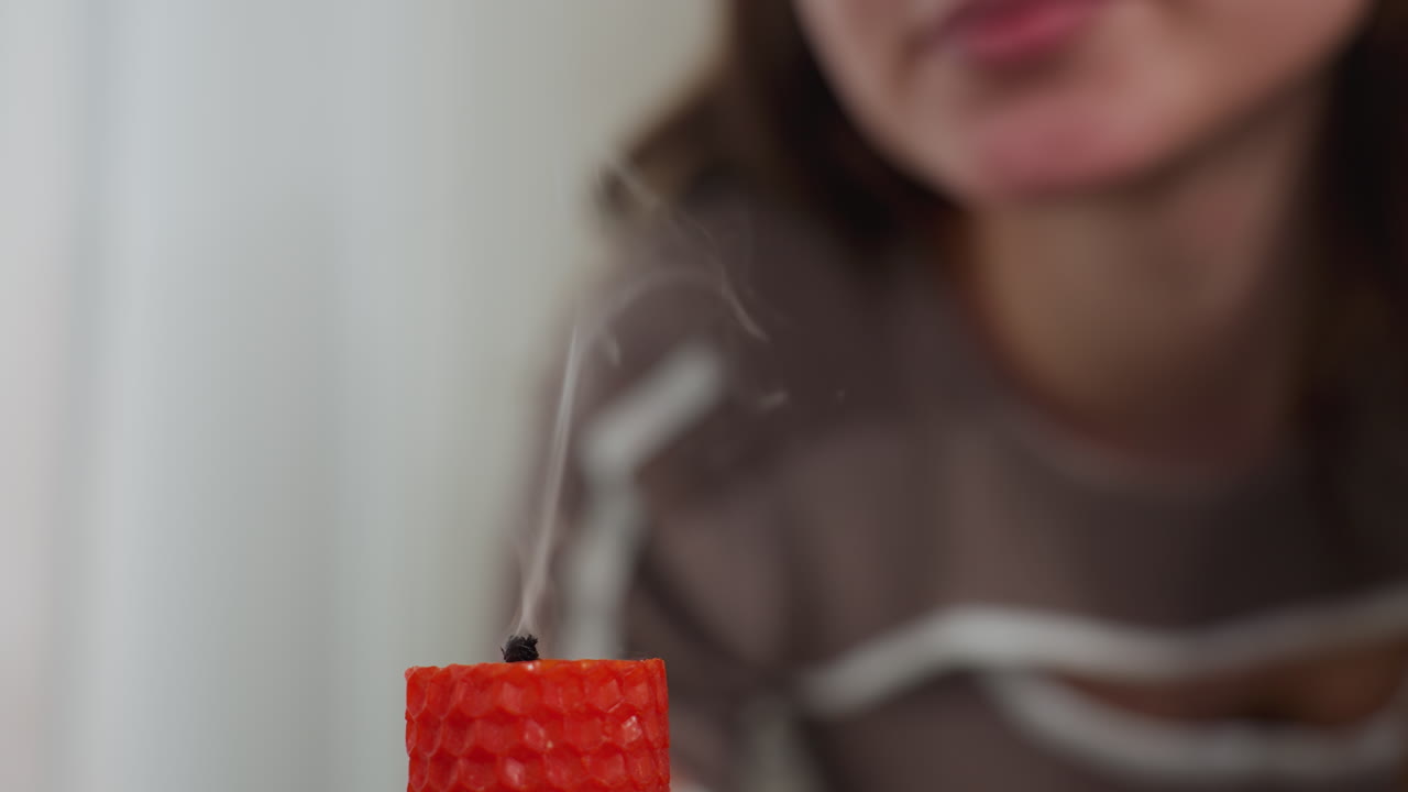 primer plano de la llama de la vela roja mientras alguien en el fondo se prepara para soplarla, el enfoque suave en la persona agrega profundidad mientras el caloroso resplandor de la llama contrasta con el entorno borroso