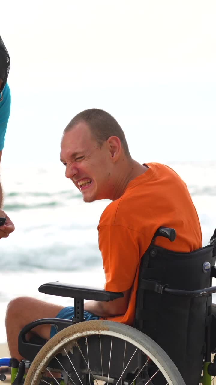 Man in wheelchair laughing with friend on the beach