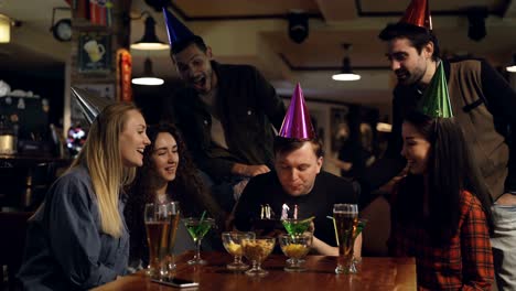 best friends are congratulating young man on birthday, he is blowing out candles on cake and thanking his mates for great party. funny holiday with friends concept.