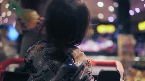 a backside slomo footage of toddler child sitting in shopping push cart and female costumer picking orange wrapped in a plastic bag in a grocery store