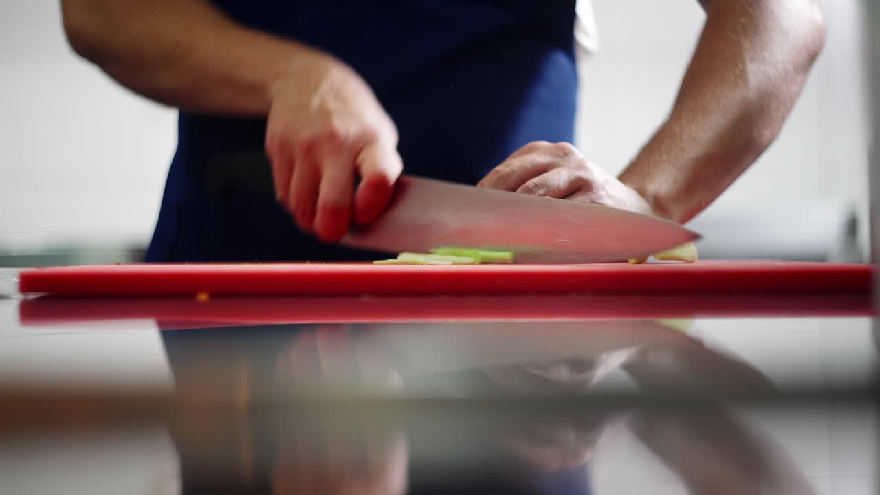 Close up view of a chef cutting celery sticks in julienne over a board.