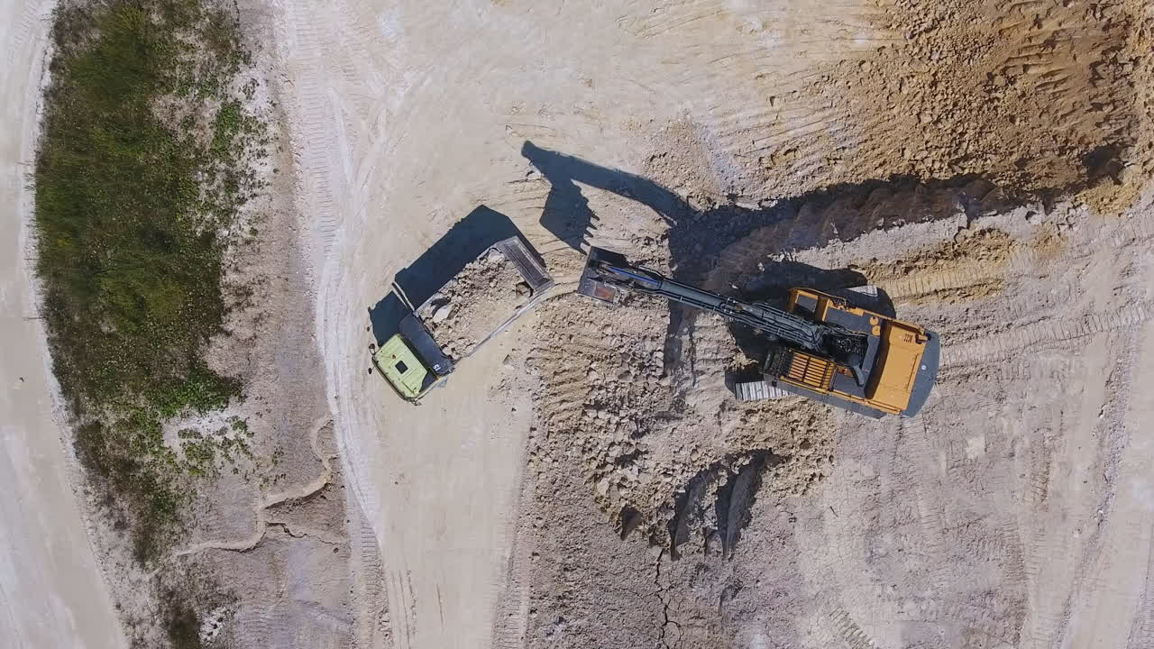 Modern excavator shoveling kaolin clay on the territory of quarry. Loaded truck leaving the site for industrial plant.