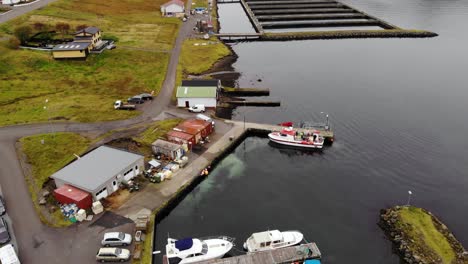 Paralaje-Aéreo-De-Un-Pequeño-Puerto-Con-Un-Barco-Rojo-Y-Blanco-En-Aguas-Tranquilas-Y-Oscuras-En-Un-Fiordo-En-Las-Islas-Feroe