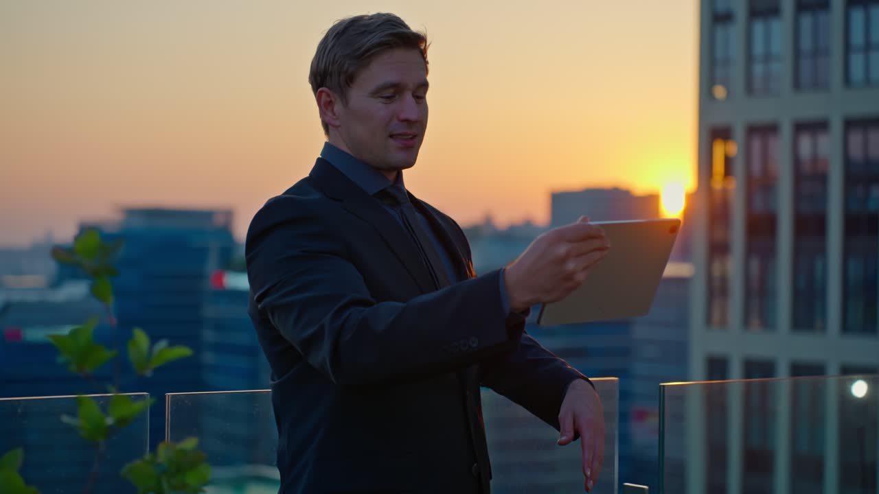 A confident and inspired Caucasian businessman smiles during a video call on a tablet, captured in a slow-motion parallax shot on a Seoul rooftop at sunset