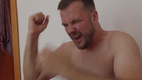shirtless man expresses extreme anger and frustration, screaming loudly with clenched hands and tense posture. strong emotional outburst captured in a dramatic close-up scene indoors