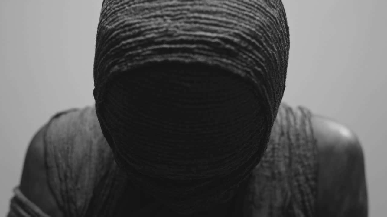 A mummy of a woman on a white backdrop slowly rises her head