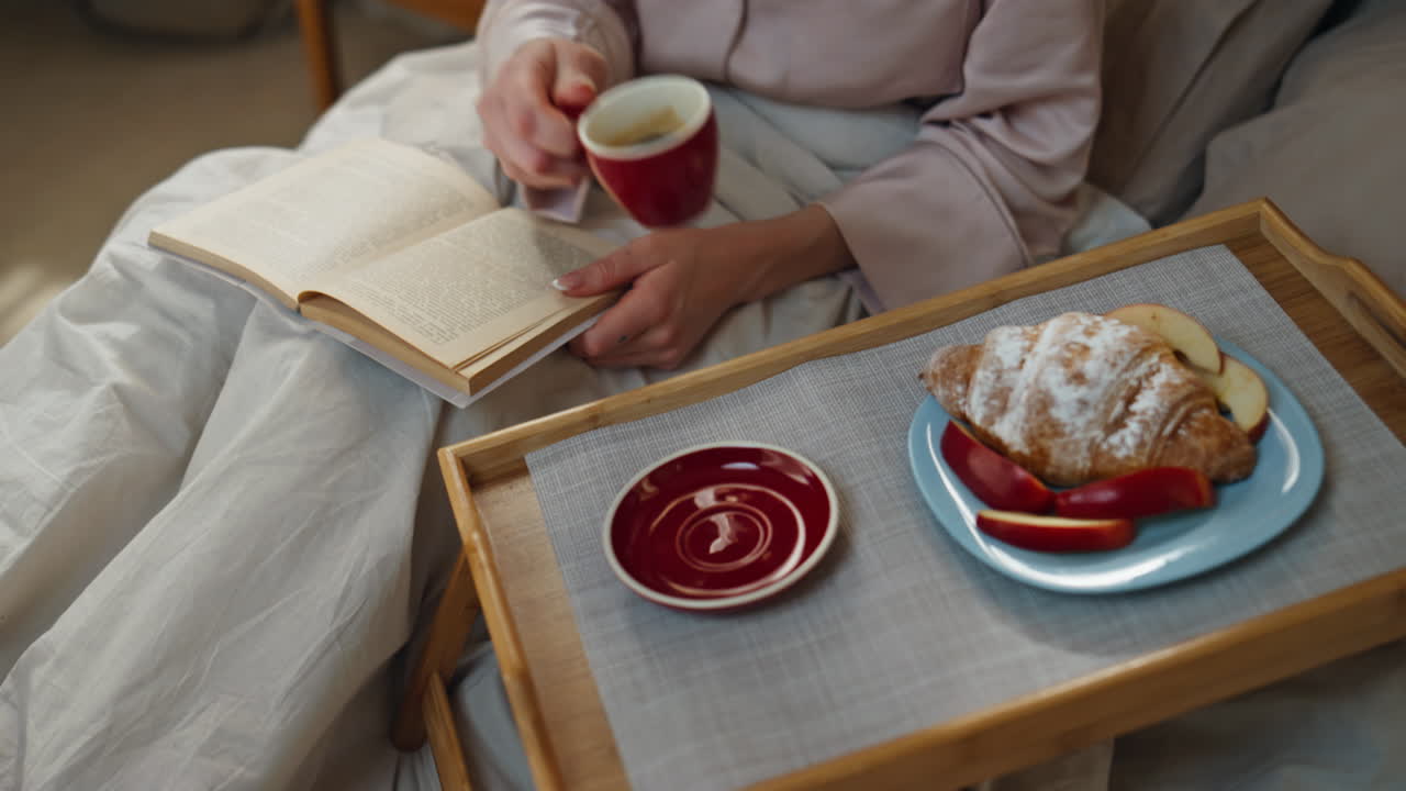 Woman enjoying breakfast in bed while reading