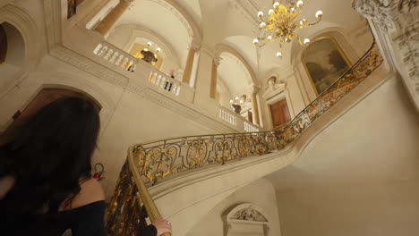 hermosa y elegante joven morena vestida con un vestido negro, subiendo una lujosa escalera del museo del louvre