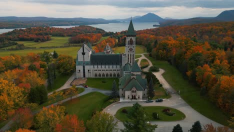 aerial-over-saint-benoit-du-lac-abbey-and-memprhemagog-lake-with-mountains-in-the-background-at-autumn-season,-magog,-quebec-region,-canada-during-fall