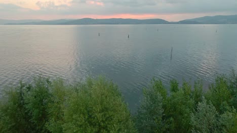 vista sobre las tranquilas aguas del lago trasimeno durante el amanecer en italia - retroceso aéreo