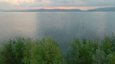 view on the calm waters of trasimeno lake during sunrise in italy - aerial pullback