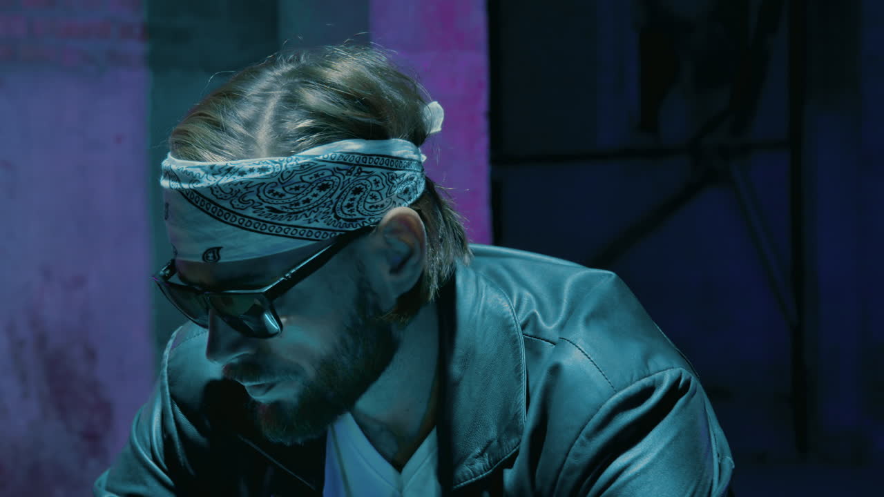 мужской байкер в бандане в солнцезащитных очках против кирпичной стены с неоновым знаком