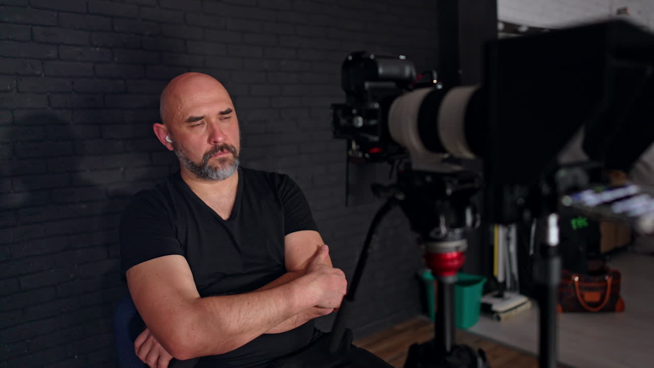 Calm relaxed bearded man in black t-shirt sits looking at camera display. Backstage of studio footage.